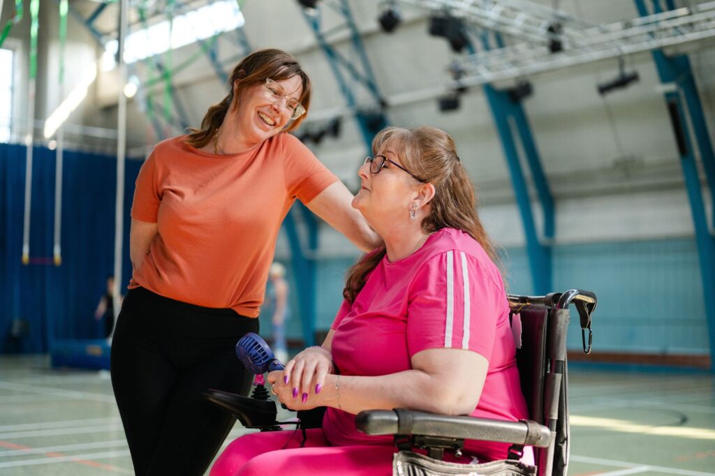 A trainer and a woman who uses a wheelchair share a laugh in the gym