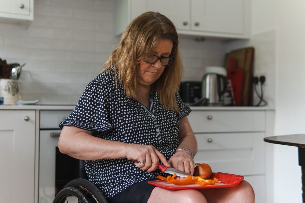 A woman in a wheelchair chops vegetables in her kitchen