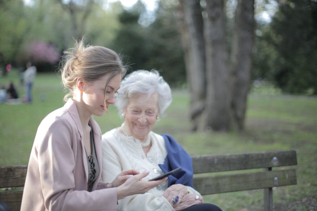 An adult daughter helps her mother with a phone in the park