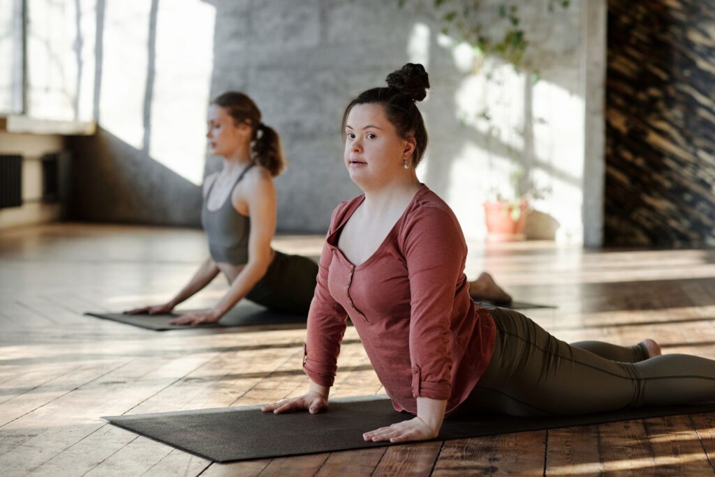 A young woman with Down syndrome holds a yoga stretch on her mat