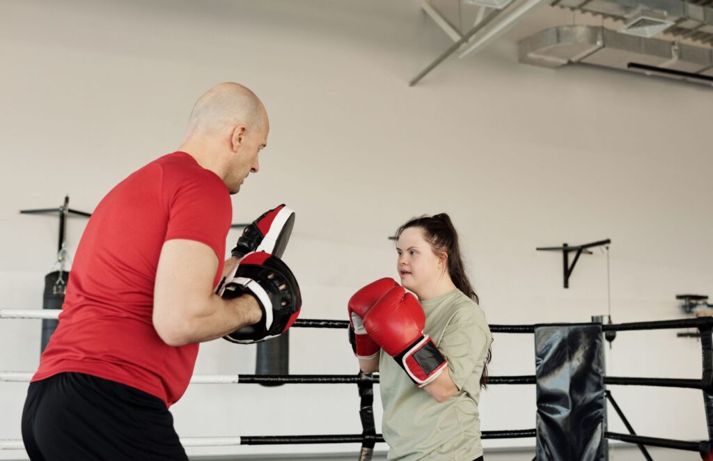 A coach guides a young woman with Down syndrome through a boxing drill