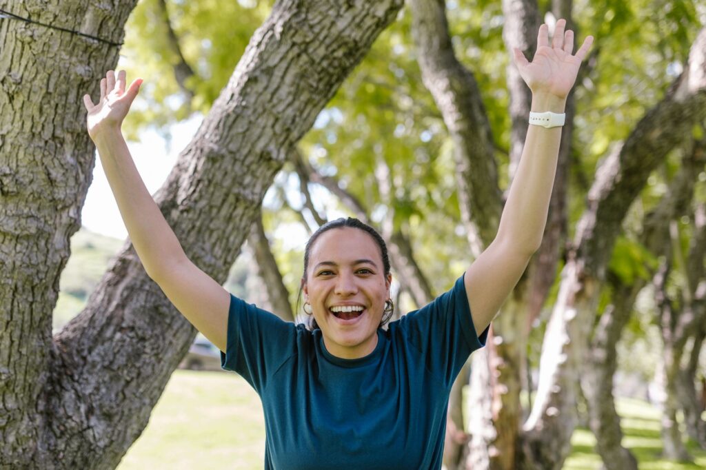 A woman raises her arms in celebration in a sunny park
