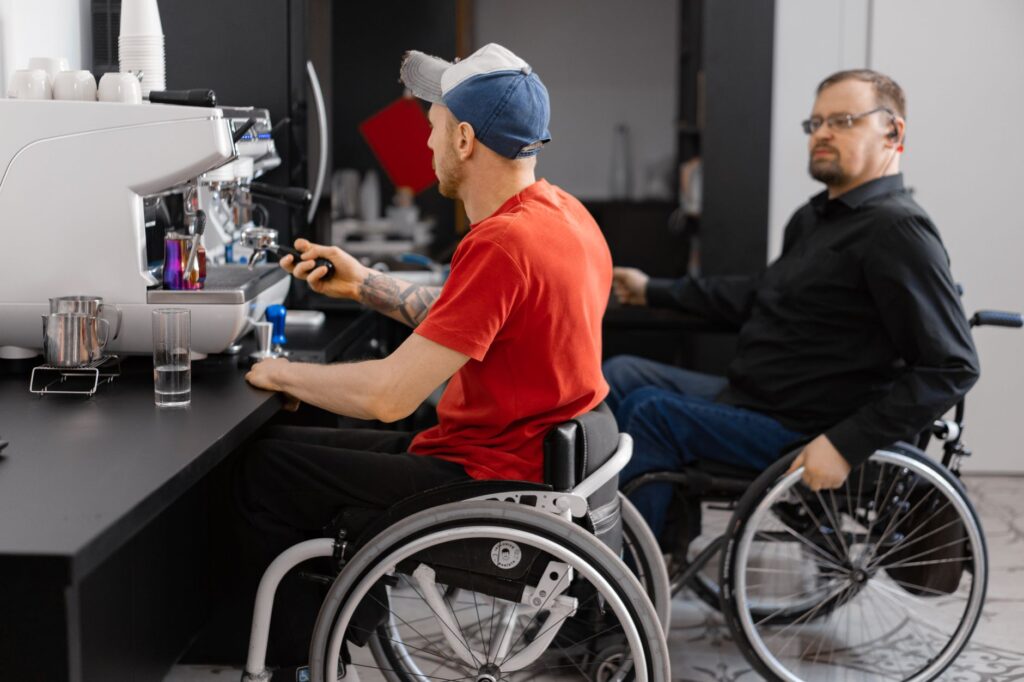 Two men who use wheelchairs work behind a coffee-shop counter