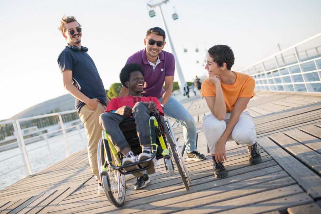 Four friends, one in a wheelchair, laugh together on a sunny deck
